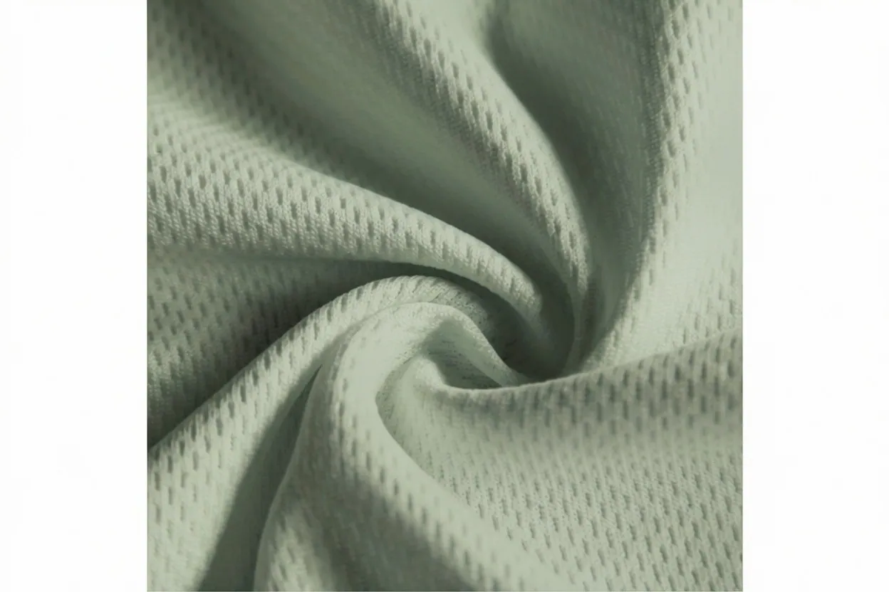 Eyelet mesh knit fabric in sage green cotton with athletic perforations, manufactured at Apex Corporation knitwear factory in Karachi Pakistan